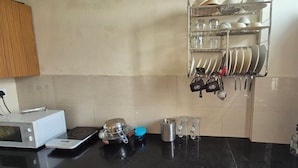 A kitchen with a microwave, a kettle, and a coffee maker on the counter. There is a rack with plates and utensils hanging on the wall. - Welcoming house (Mohali)