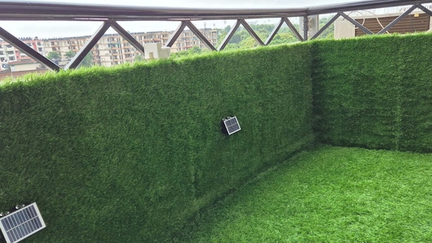 A balcony with a green artificial grass wall, metal railings, and a view of buildings in the background. - Welcoming house (Mohali)