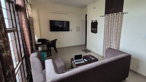 A living room with a sofa, a coffee table with a laptop, a TV, and a curtain. - Welcoming house (Mohali)