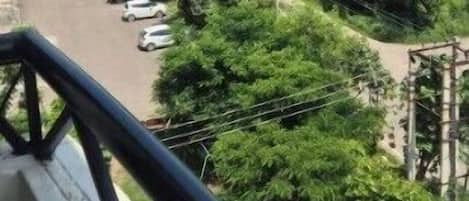 A balcony with a view of a parking lot and greenery.
