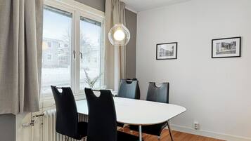 Un coin repas avec une table blanche, quatre chaises noires, un luminaire suspendu et deux tableaux encadrés accrochés au mur.