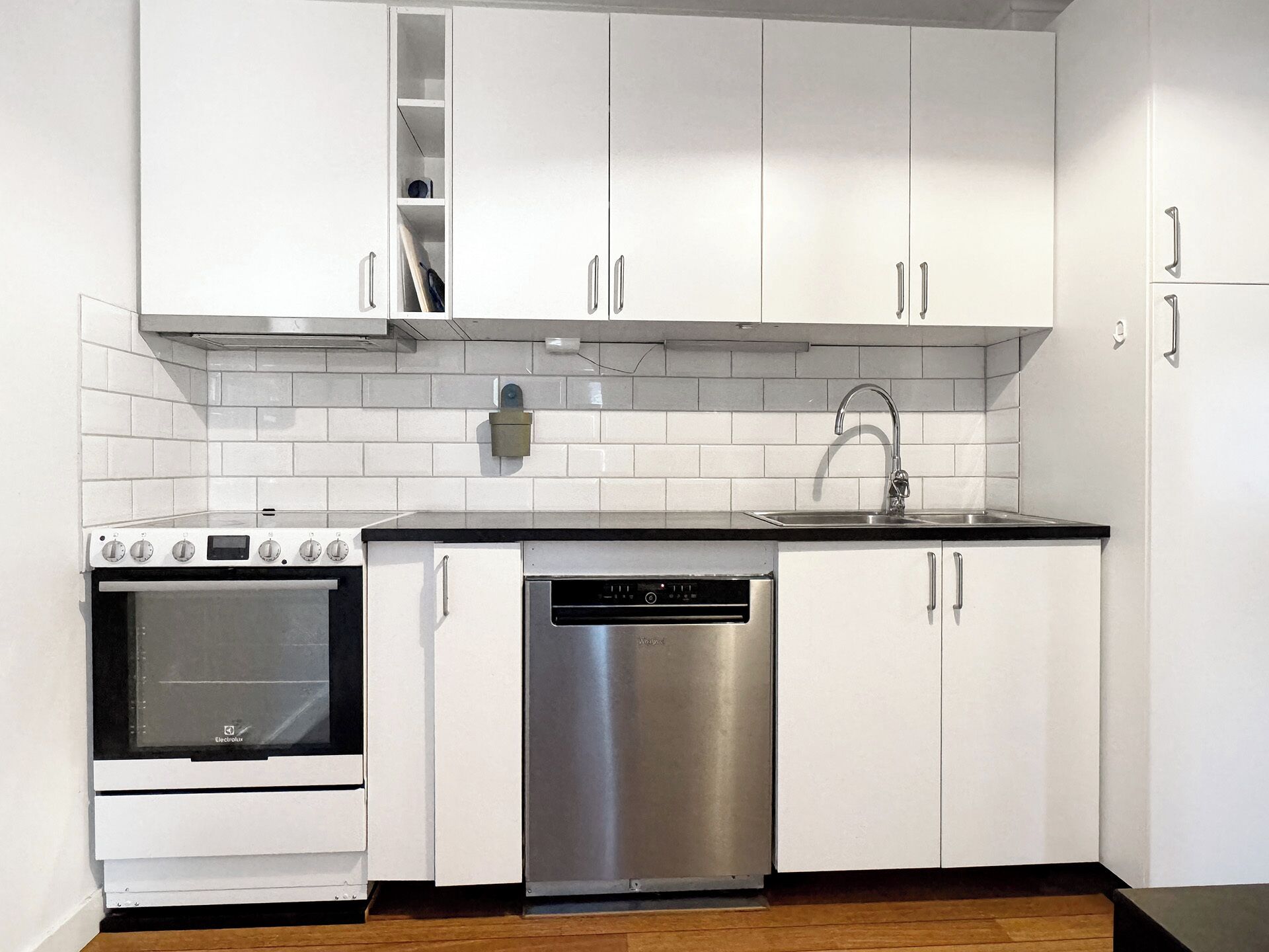 A modern kitchen with white cabinets, a stainless steel dishwasher, and a built-in oven.