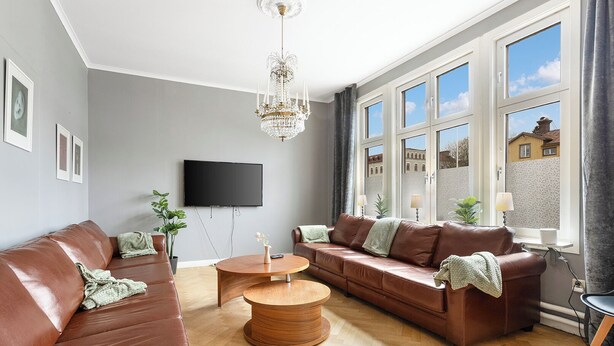A modern living room with a brown leather sofa, a wooden coffee table, and a chandelier. - HernöRum - Fiskekroken (Harnosand)