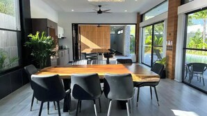 A modern dining area with a large wooden table and black chairs, large windows, and a view of the outdoors.