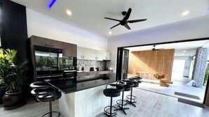 A modern kitchen with a black countertop, white cabinets, and a built-in oven. There are four black bar stools with metal frames and black seats. A ceiling fan is visible above the kitchen.