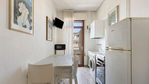 A compact kitchen with a dining table, chairs, a washing machine, a refrigerator, and a television.