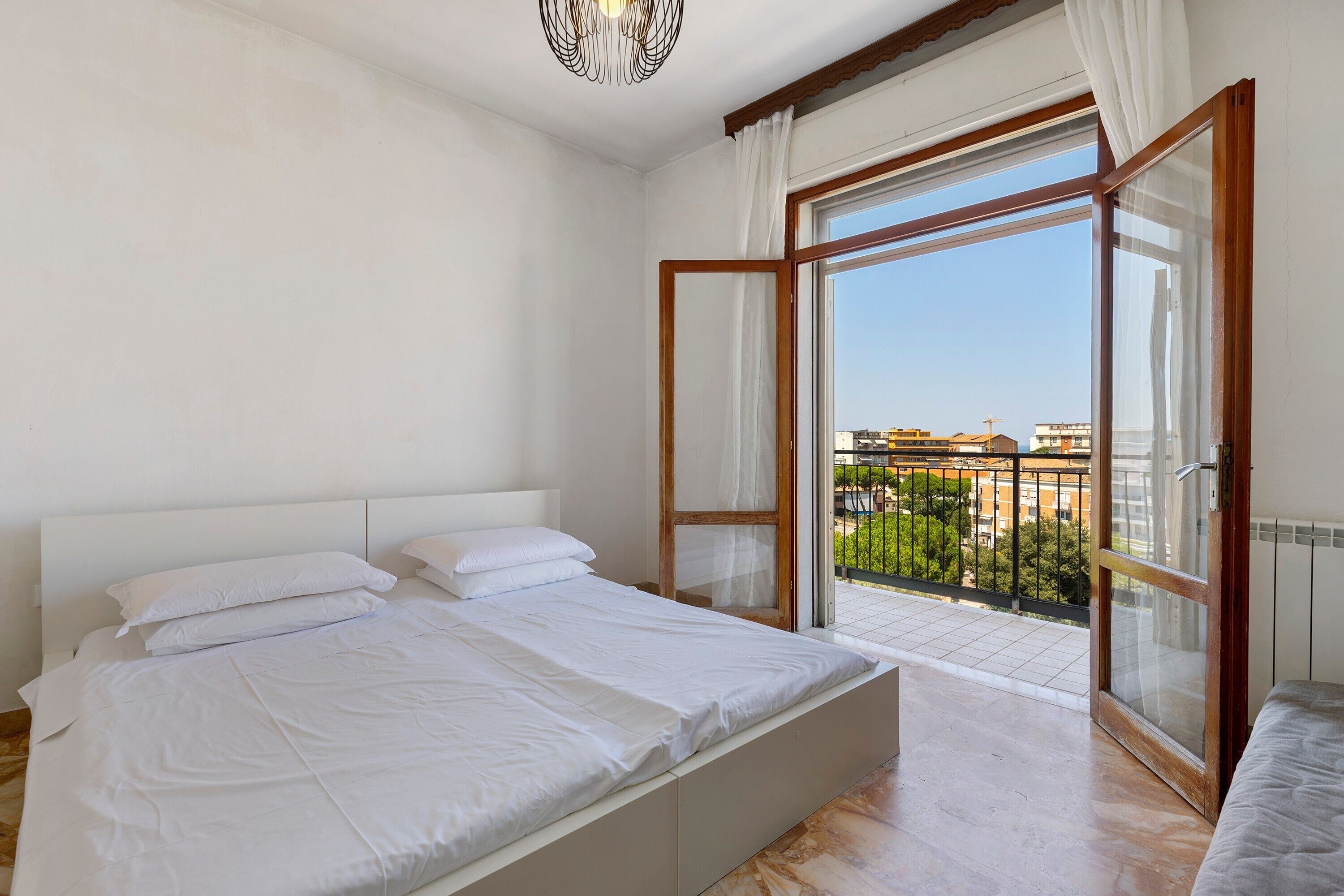 Une chambre dotée d’un grand lit, d’une porte-fenêtre coulissante donnant sur un balcon et offrant une vue sur les immeubles.