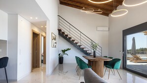 A modern interior with a staircase, a dining area with green chairs, and a large window offering a view of the outdoors.