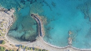 An aerial view of a coastal area with clear blue waters, rocky shorelines, and a sandy beach.