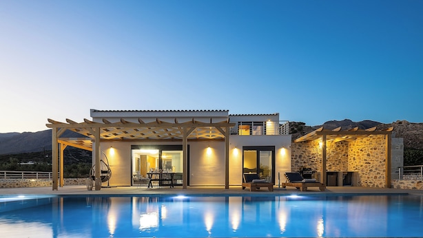 A modern villa with a swimming pool, outdoor seating, and a stone wall.