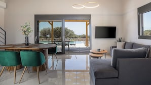A modern living room with a dining area, a large TV, and a view of the outdoors.