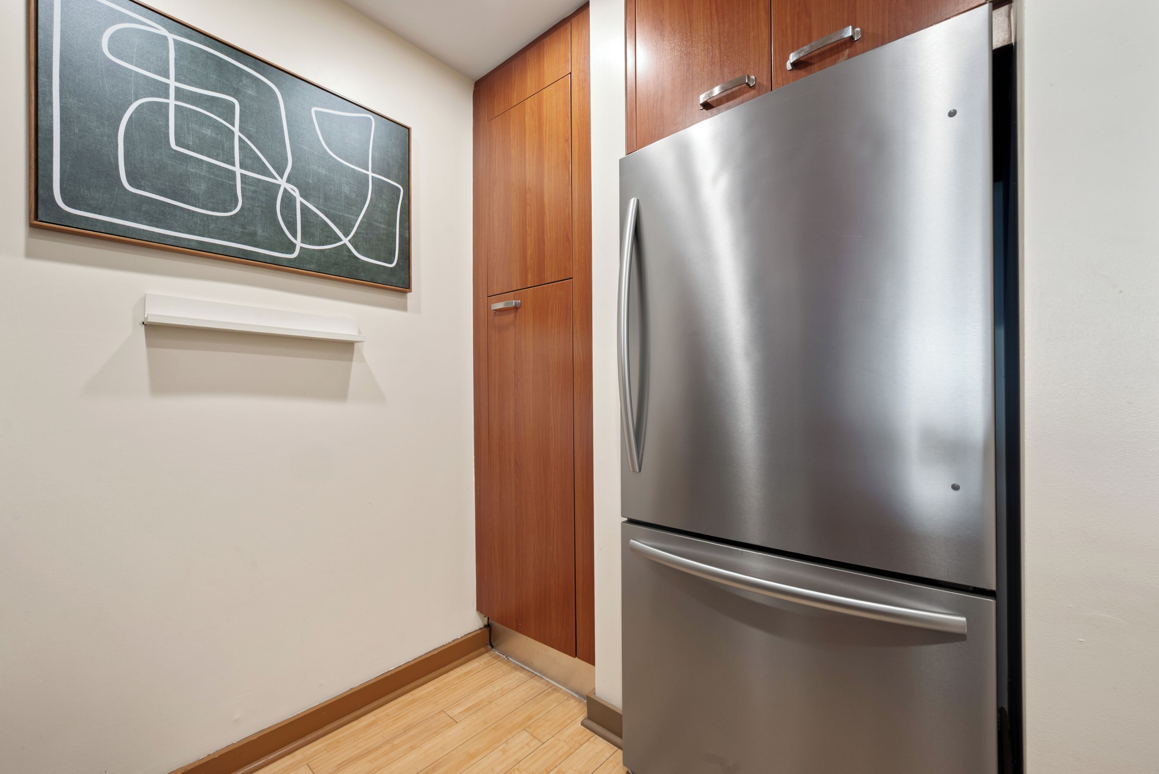 A kitchen with a stainless steel refrigerator, wooden cabinets, and a wall-mounted abstract art piece.