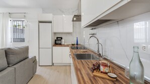 Una cocina moderna con armarios blancos, encimera de madera, microondas integrado y pileta de acero inoxidable.