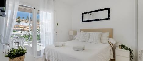 Ein Schlafzimmer mit Bett, Nachttisch, Stuhl, einem Balkon und Blick auf Gebäude.
