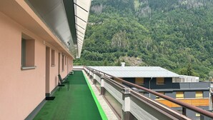 Ein Korridor mit grünem Teppich, Metallgeländern und Blick auf einen bewaldeten Berg.