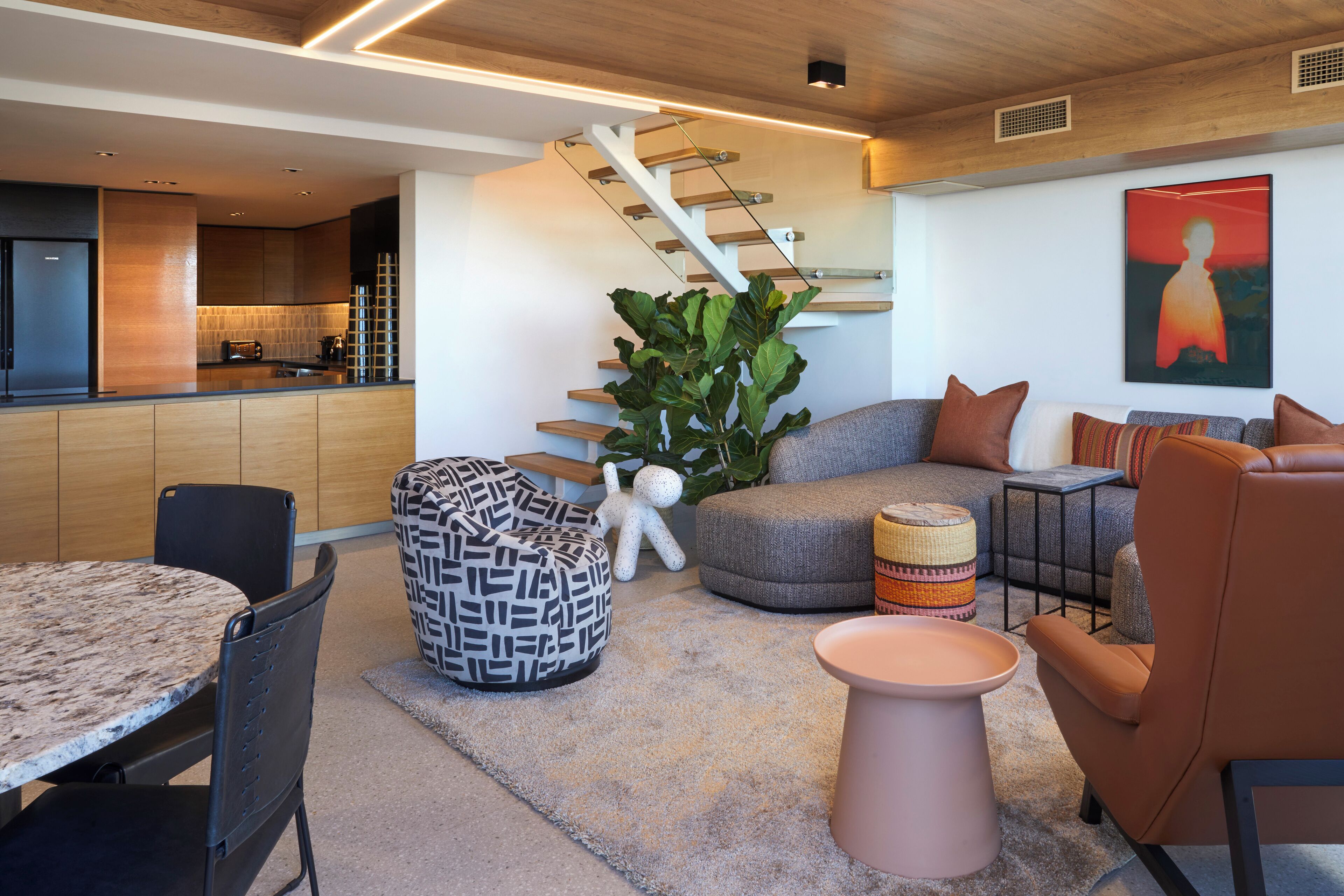A modern living area with a kitchen, a staircase, and seating arrangements.