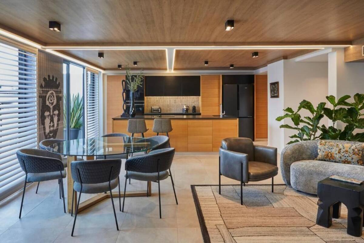 A modern kitchen with a central island, a dining area with a glass table and chairs, and a living area with a sofa and a coffee table.