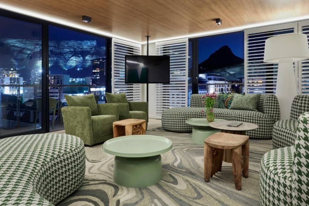 A modern living room with a large TV, green and houndstooth patterned furniture, and a view of a cityscape at night.