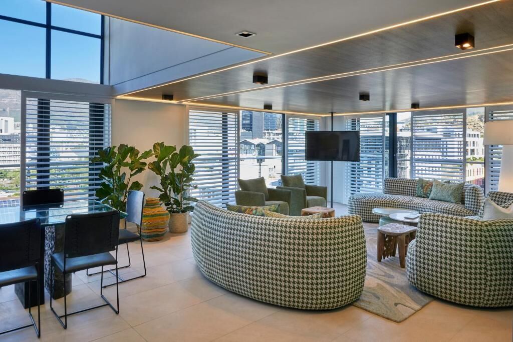 A modern living room with a glass dining table, comfortable seating, and large windows offering a city view.