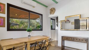 A dining area with a wooden table and chairs, a large window with a view of greenery, a wall-mounted clock, and a console table with drawers. - Country House 'La Zua' with Private Pool, Wi-Fi and Air Conditioning (Villamartin)