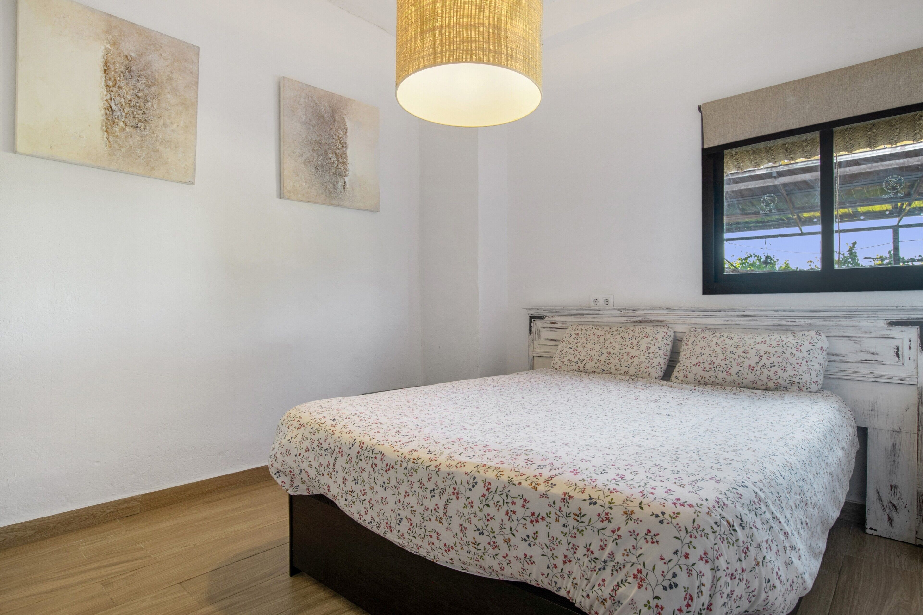 A bedroom with a bed, a window, and artwork on the wall.