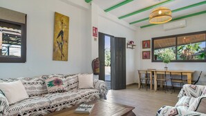 A living room with patterned sofas, a wooden coffee table, a dining area with a table and chairs, and a large window with a view of greenery. - Country House 'La Zua' with Private Pool, Wi-Fi and Air Conditioning (Villamartin)