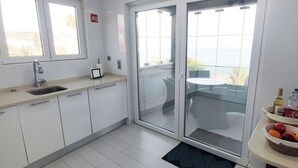 A modern kitchen with a sink, countertop, and a view of the sea through a sliding glass door. - Casa do Mar - Luxury Villa w rooftop SwimSpa (Luz)