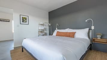 A modern bedroom with a large bed, a bedside table with a lamp, a wall-mounted shelf, and a framed picture on the wall.