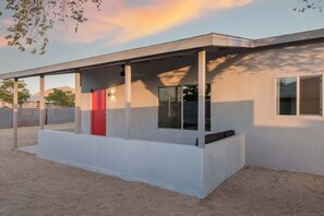 Un bâtiment moderne doté d’un espace extérieur abrité, de grandes fenêtres et d’une porte rouge.