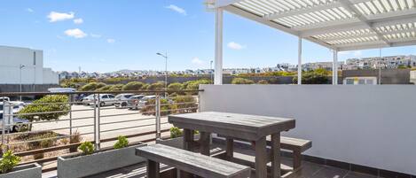 A rooftop terrace with a wooden table and bench, a covered area, and a view of a residential area.