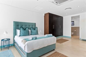 Un dormitorio moderno con una cama tapizada en color turquesa, ropa de cama blanca y un armario de madera.