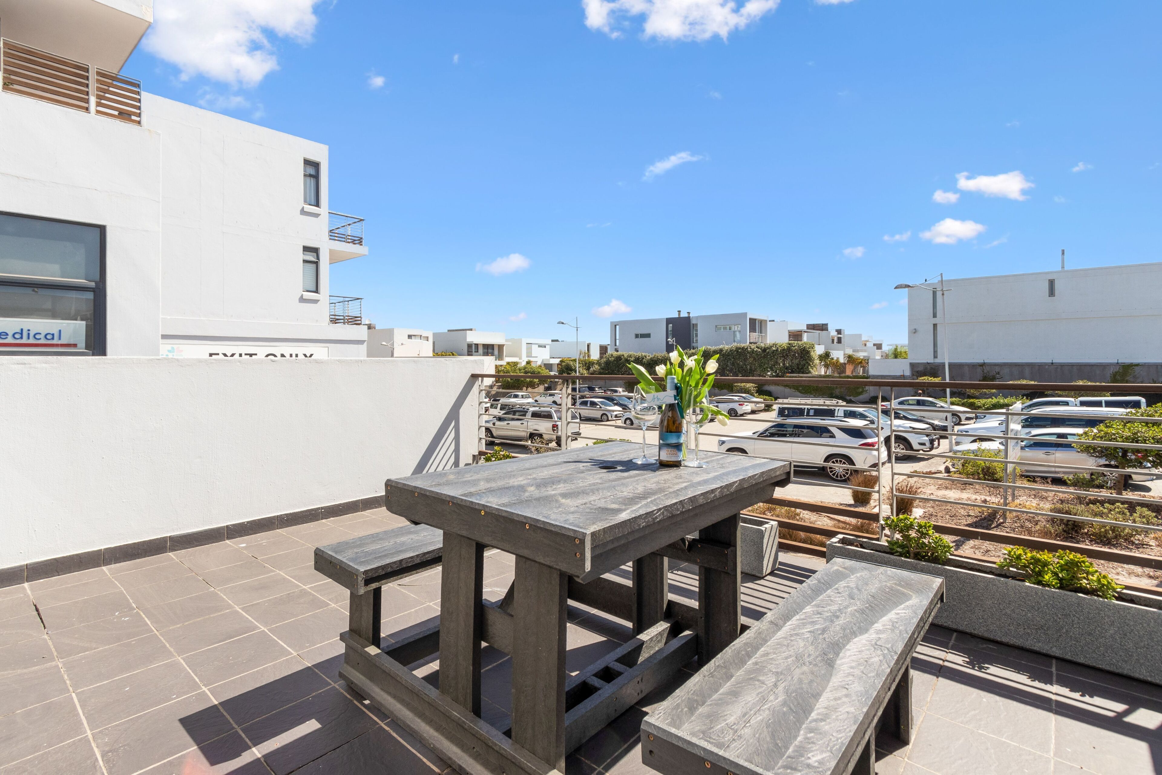 Eine Dachterrasse mit Tisch und Bänken, im Hintergrund ein Parkplatz und ein strahlend blauer Himmel.