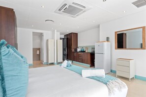 Una habitación de hotel moderna con una cama grande, una kitchenette, un baño y un espejo.