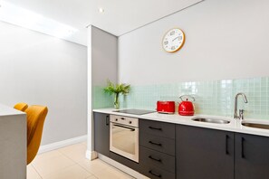 A modern kitchen with a built-in oven, a double sink, and a red kettle. - Eden on the Bay 190 (Cape Town)