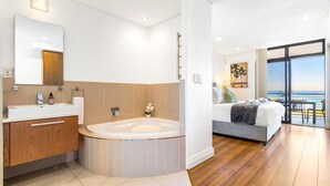 Et moderne hotelværelse med et stort badekar, en seng med udsigt og en balkon med et bord og stole.