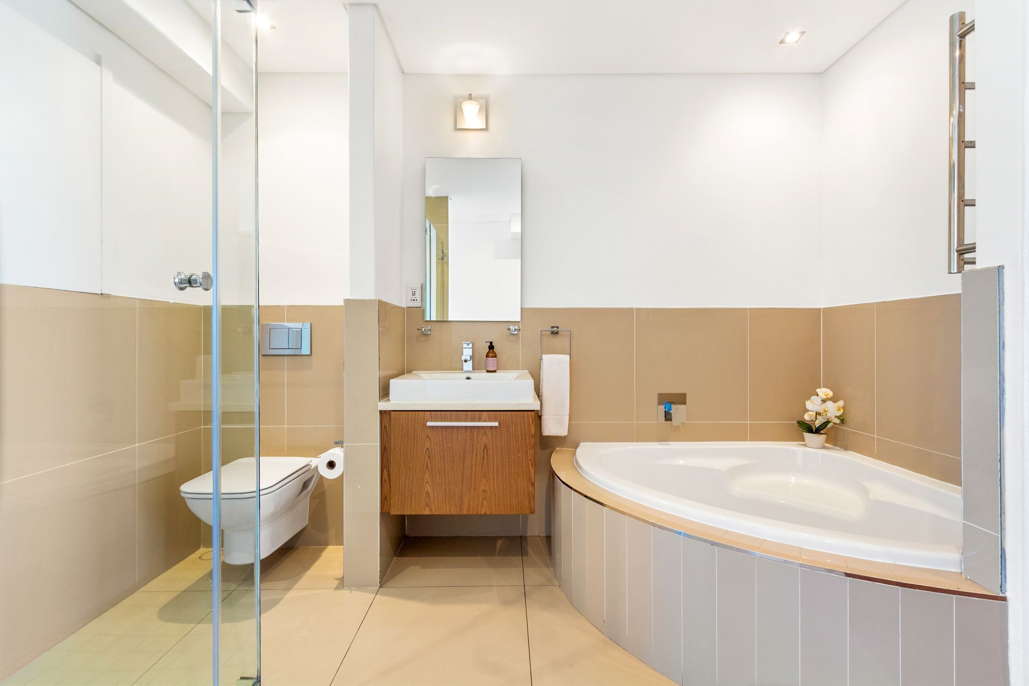 Ein modernes Badezimmer mit Duschkabine aus Glas, Toilette, Waschbecken mit Holzschrank und einer großzügigen Badewanne.