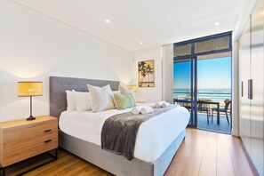 A modern bedroom with a large bed, a nightstand, and a view of the ocean through a sliding glass door. - Eden On The Bay 168 (Cape Town)