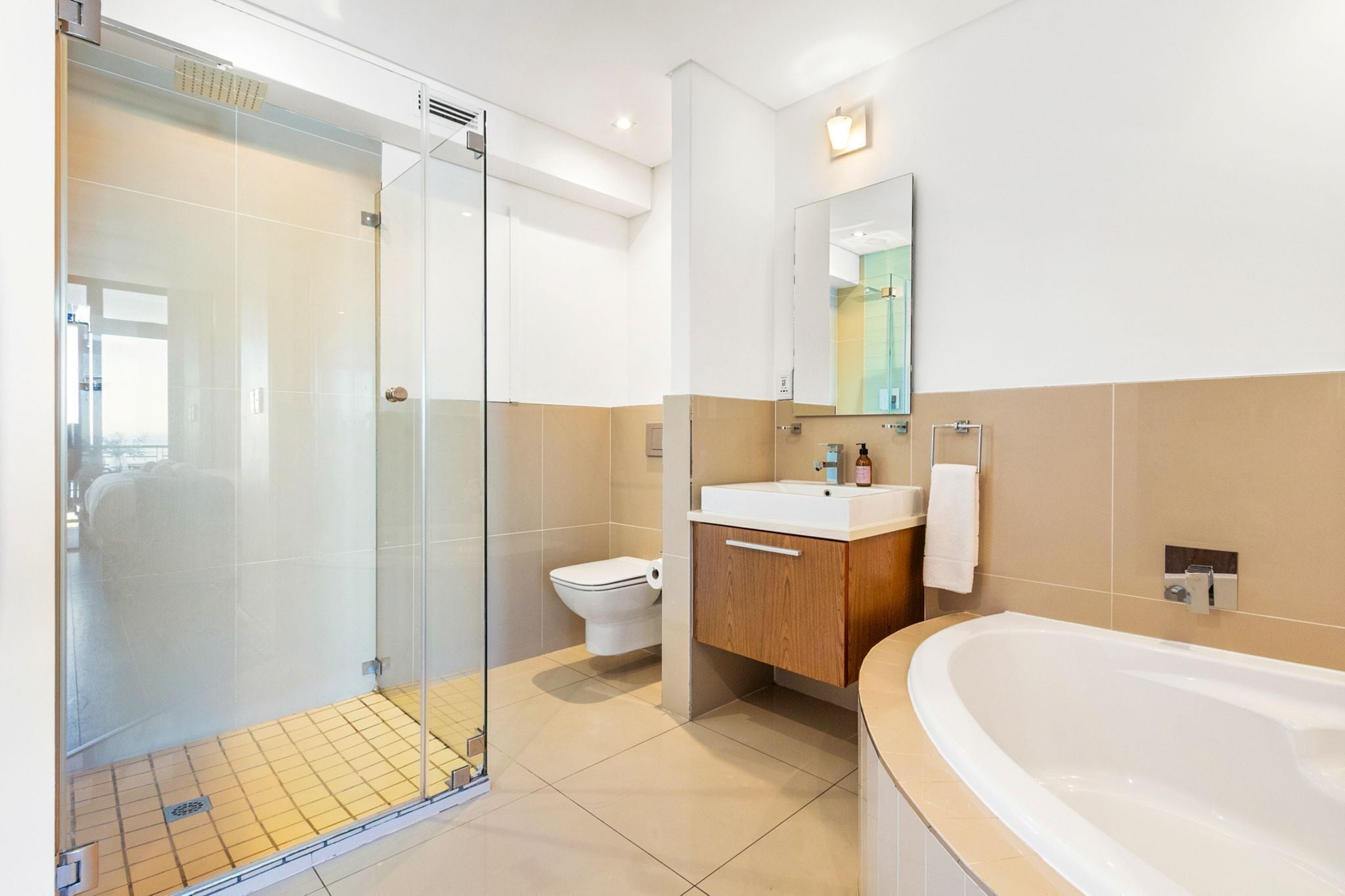 A modern bathroom with a glass shower enclosure, a toilet, a sink with a mirror, and a bathtub.