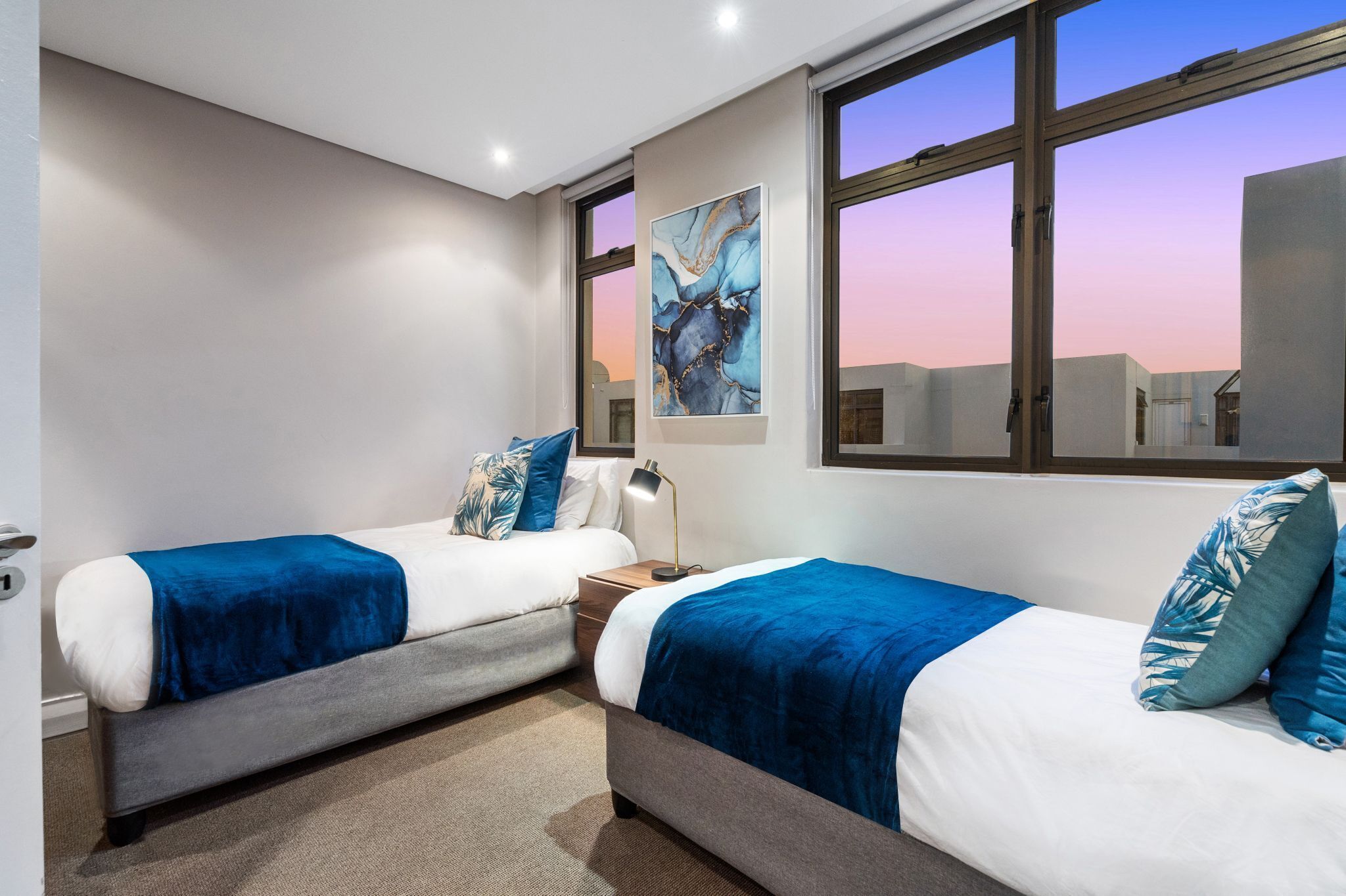 Une chambre d’hôtel avec deux lits, une grande fenêtre et un tableau au mur.