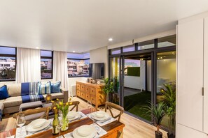 A modern living room with a dining area, large windows, and a view of the cityscape. - Eden On The Bay 102 (Cape Town)