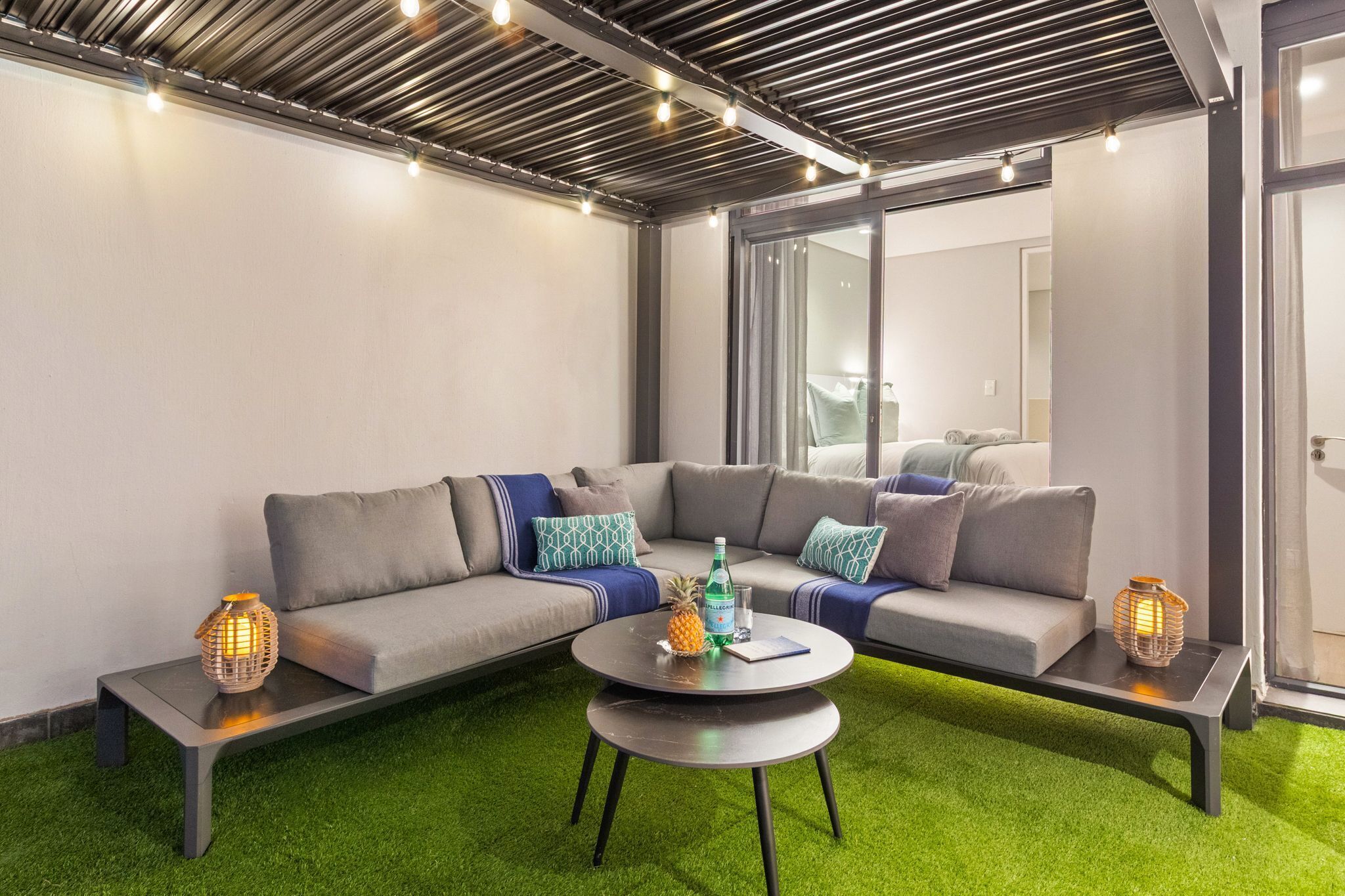 Un área de estar moderna con un sofá modular, una mesa de centro redonda y dos mesitas de noche con faroles decorativos.