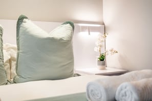 A neatly made bed with a light green pillow, a bedside table with a small potted plant, and rolled white towels. - Eden On The Bay 102 (Cape Town)