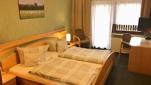 Ein Hotelzimmer mit zwei Betten, einem Schreibtisch, einem Stuhl, einem Fernseher und einem Fenster mit Vorhängen.