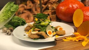 Ein Teller mit Essen, darunter Salat, Eier und Hackbällchen, umgeben von Gemüse und einem Kürbis.
