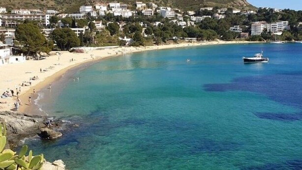 Un pueblo costero con una playa de arena, aguas azules cristalinas y edificios en una ladera.