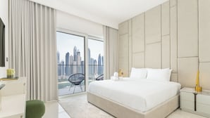 A modern hotel room with a large bed, a city view, and a balcony with a chair.