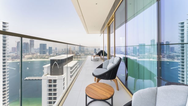 A balcony with a city view, a chair, a table, and a glass railing.