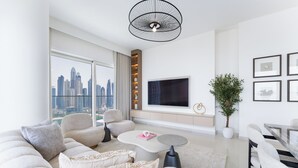 A modern living room with a large sofa, a coffee table, and a TV. There's a city view through large windows, and a plant is on the right.