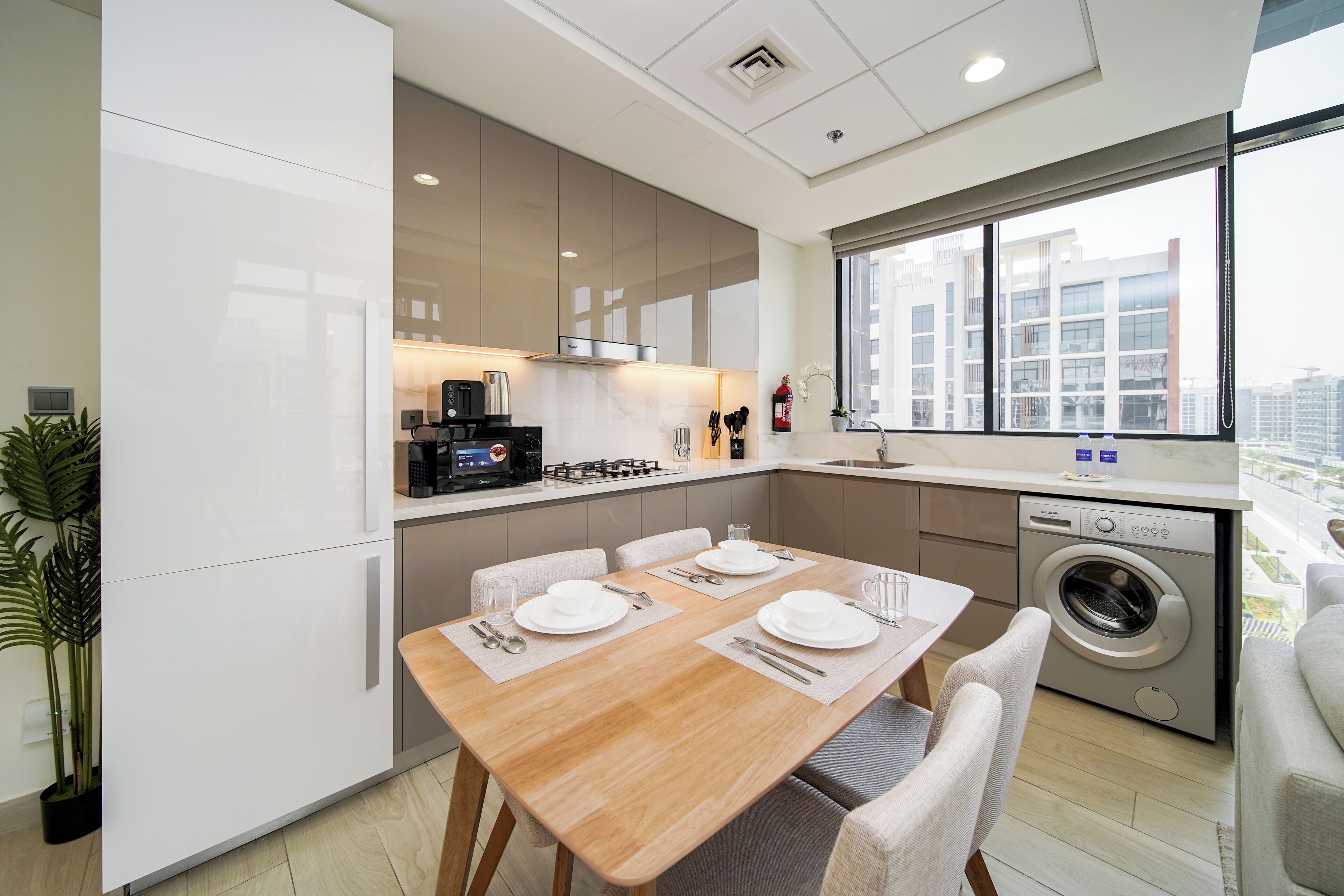 A modern kitchen with a dining area, built-in appliances, and a large window offering a city view.