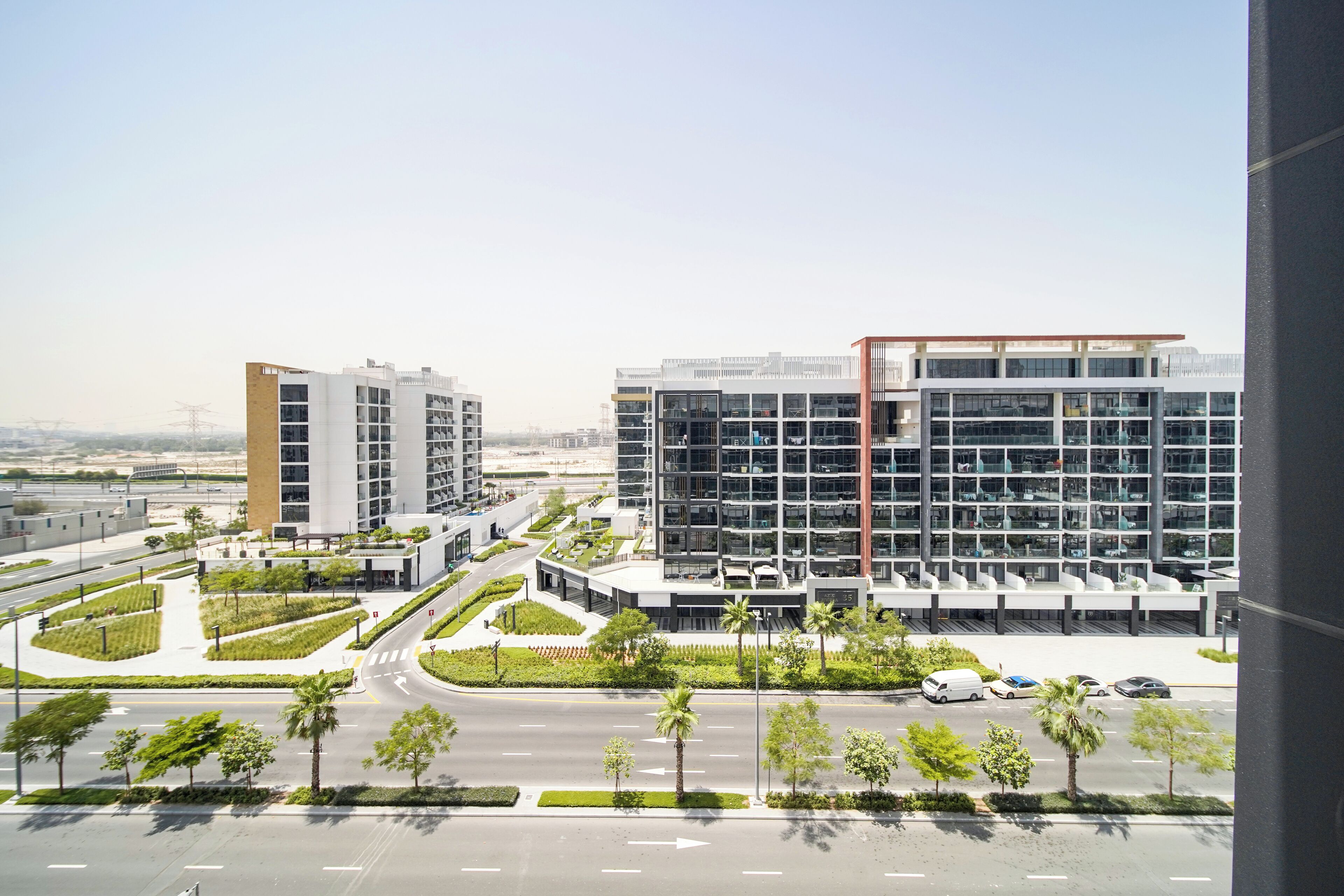 A modern building complex with multiple floors, a parking area, and a landscaped area with palm trees.